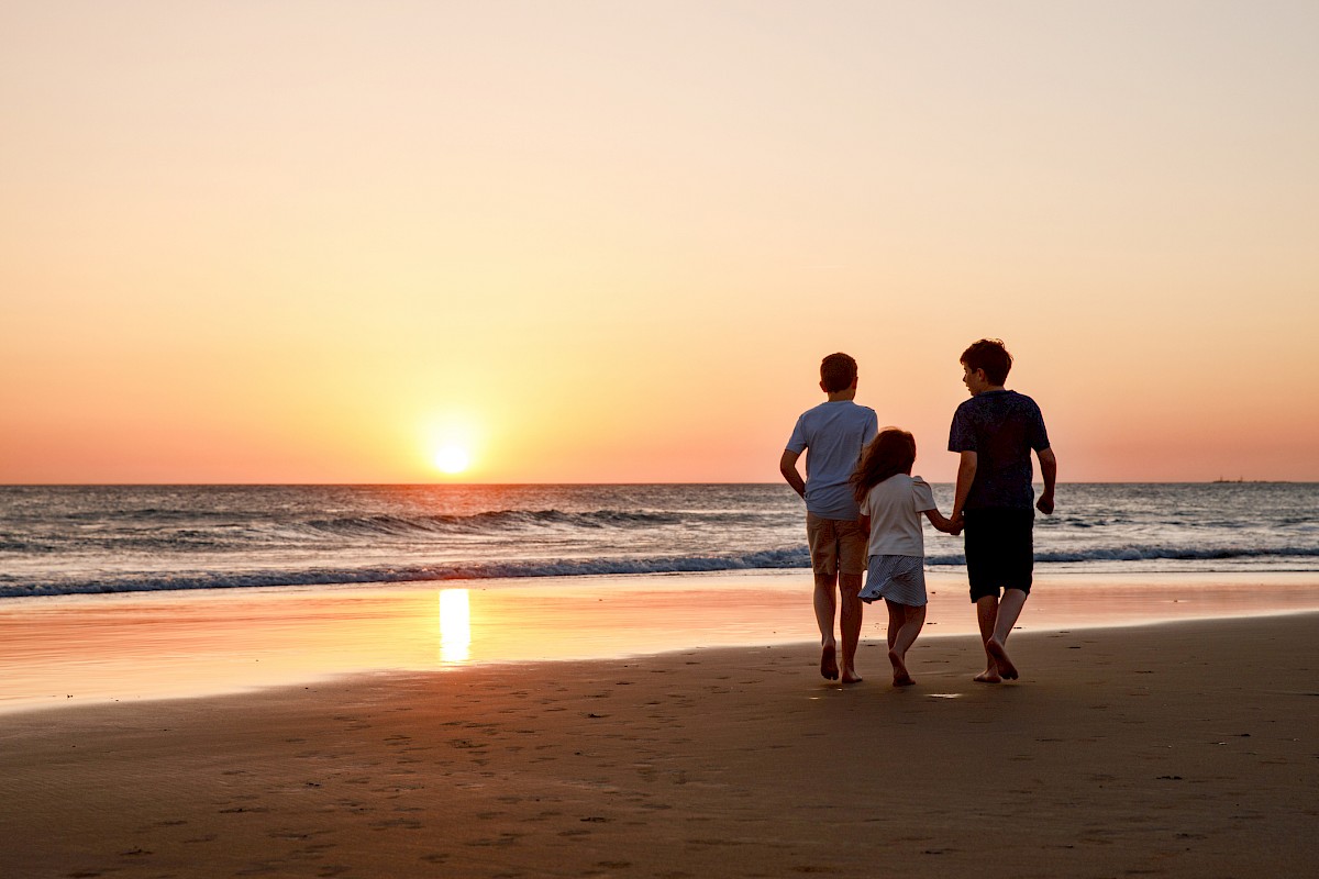 Three kids silhouettes running and jumping on beach at sunset. happy family, two school boys and one little preschool girl. Siblings having fun together.