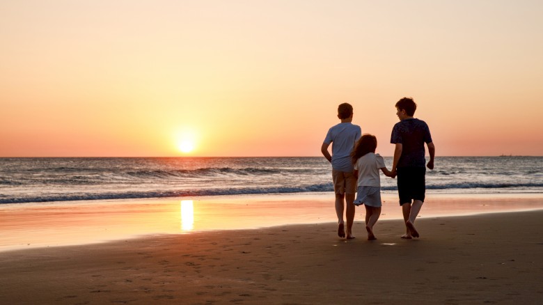 Three kids silhouettes running and jumping on beach at sunset. happy family, two school boys and one little preschool girl. Siblings having fun together.