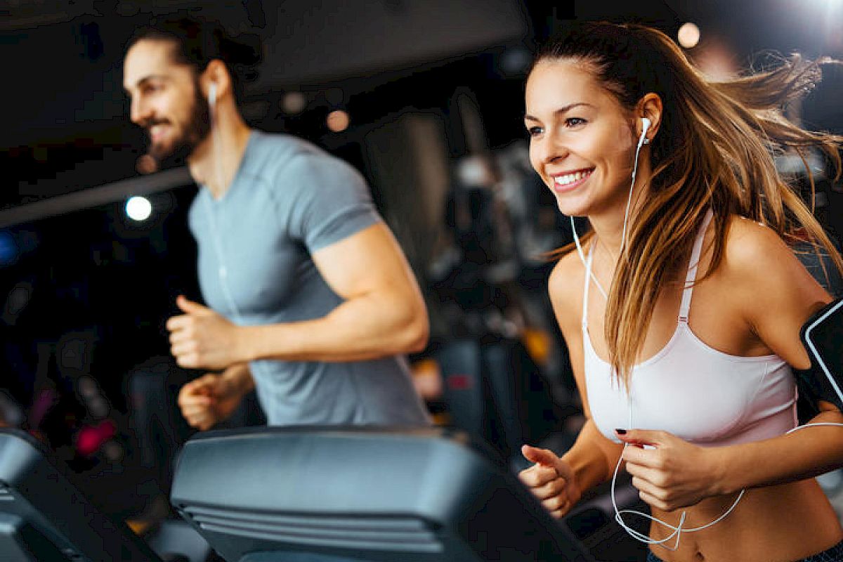 Two people are running on treadmills in a gym, looking happy and focused.