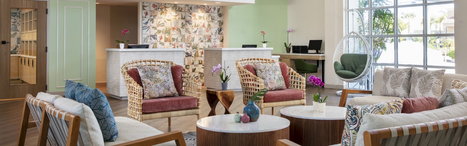 A modern lobby with chairs, cushions, reception desk, and large windows.