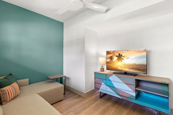 Modern living room with a couch, colorful TV stand, and a mounted television displaying a beach scene.