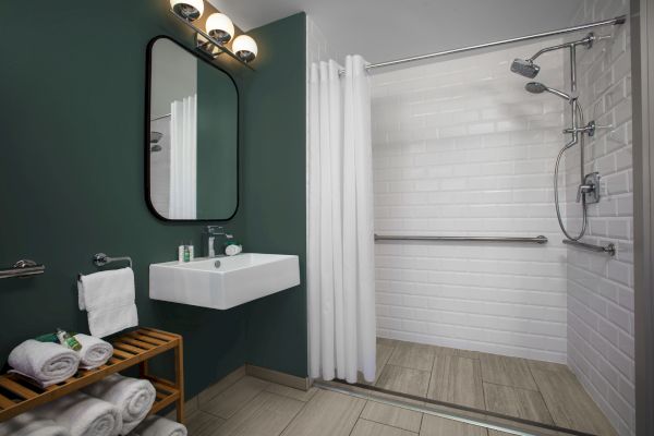 A modern bathroom with a shower, white towels, sink, mirror, and dark green walls.