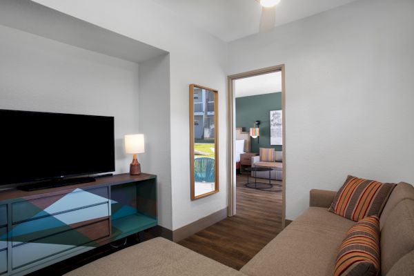 Modern living room with TV, couch, and view into another room with a desk.