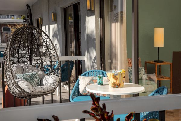 A cozy balcony with a hanging egg chair, table, drinks, and soft lighting.