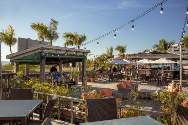 Outdoor patio with people dining, string lights overhead, and lounge furniture.