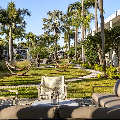 The image shows an outdoor lounge area with seating, hammocks, palm trees, and manicured grass, adjacent to a building with balconies.