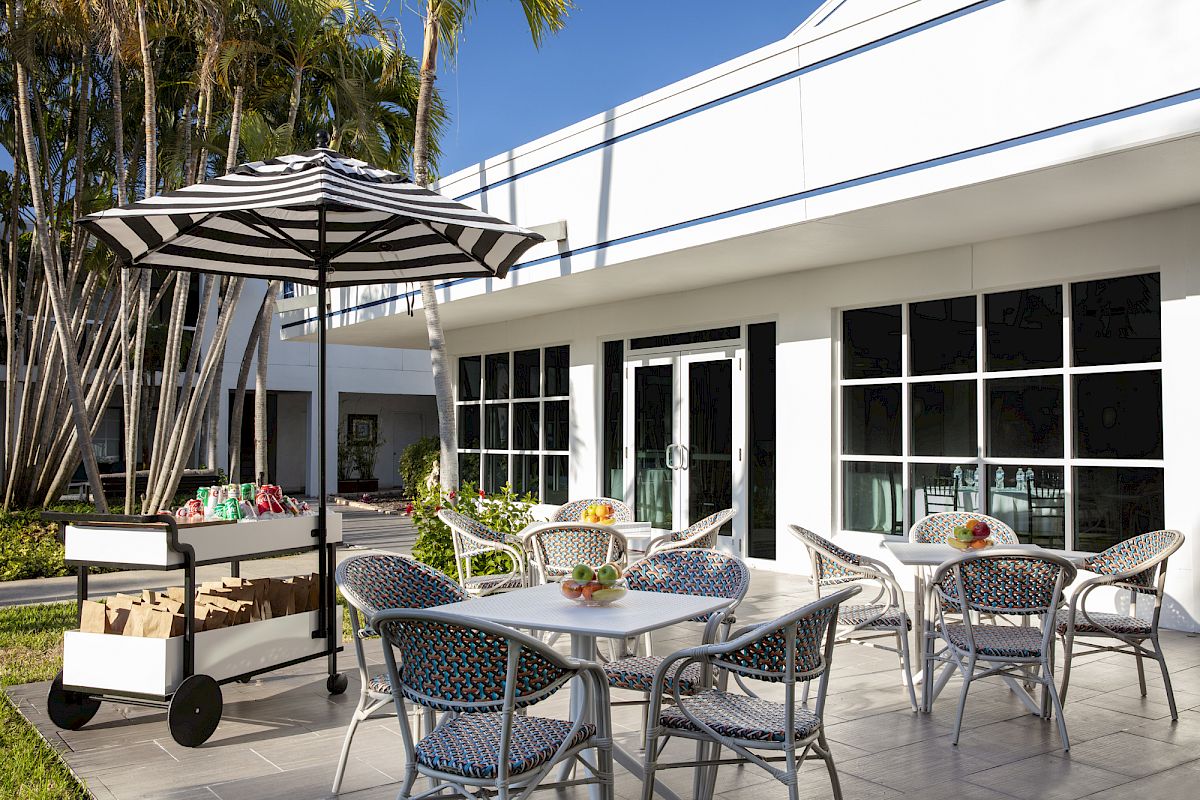 Beachcomber's outdoor patio with tables and chairs, a black-and-white striped umbrella, lush greenery, and a white building in the background.