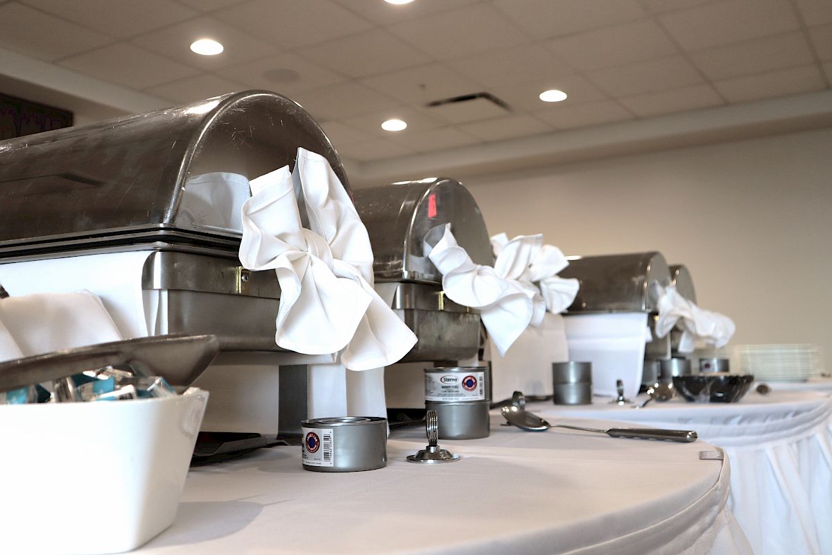 Chafing dishes with white cloth decorations on a buffet table, along with various condiments and utensils, are seen in the image.