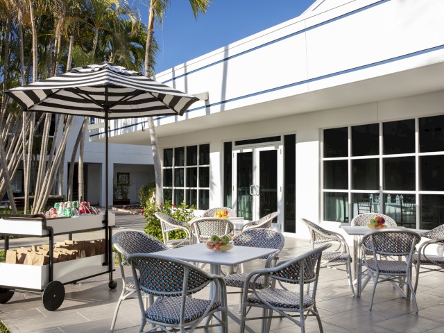 A sunny patio with chairs, a table, umbrella, and a food cart.