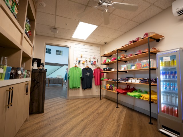 A small shop with clothes, shoes on shelves, and a fridge with drinks.