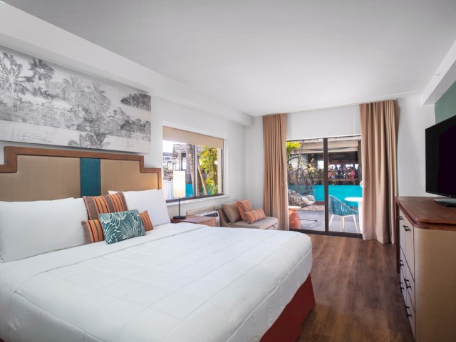Elegant hotel room with a large bed, sofa, TV, and sliding doors leading to a pool view.