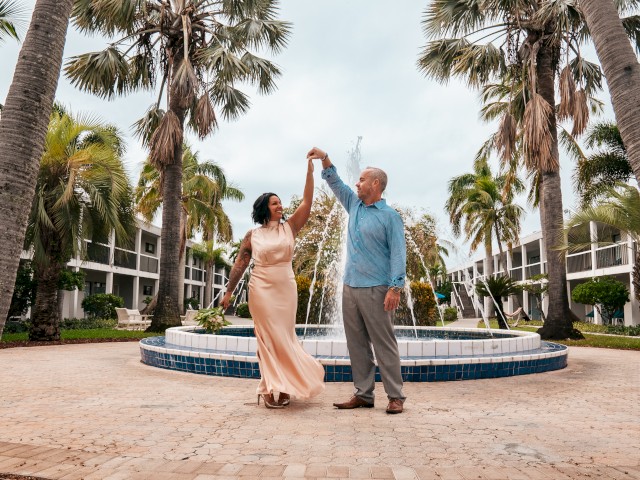 A couple dances near a fountain surrounded by palm trees.