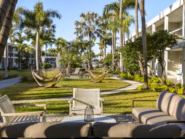 Sunny resort view with hammocks, palm trees, outdoor furniture, and a manicured lawn.