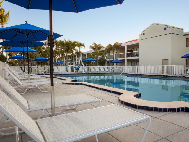 A tranquil pool area with blue umbrellas, lounge chairs, and palm trees.