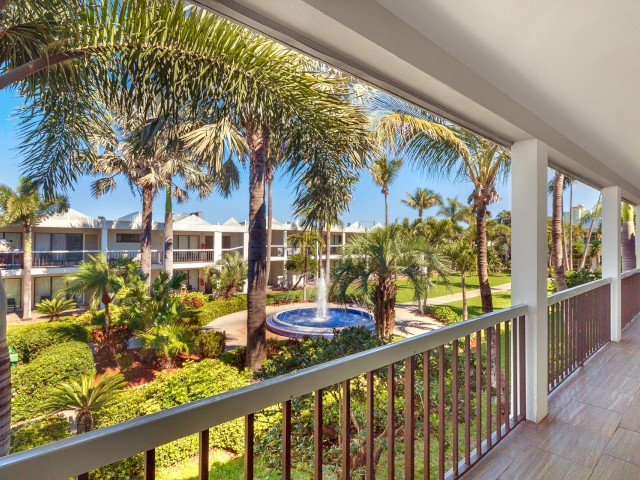Balcony view of a tropical resort with palm trees and a pool.