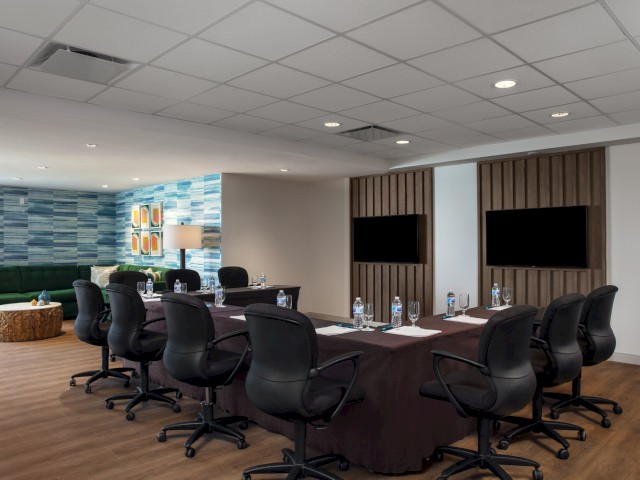 Modern meeting room with a table, chairs, and two flat-screen TVs on the wall.