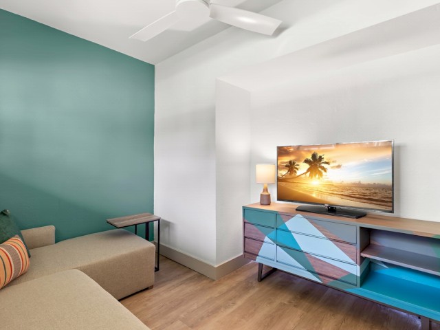 Modern living room with a sofa, colorful TV stand, and a ceiling fan.