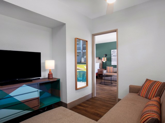 Modern living space with TV, couch, and a glimpse of dining area through doorway.