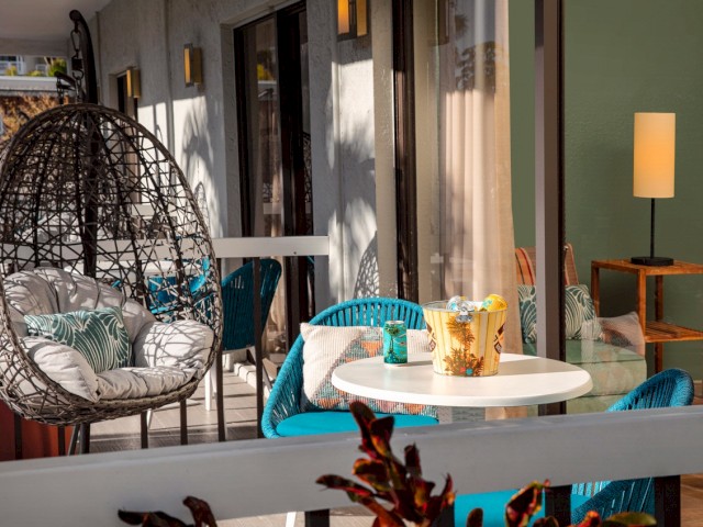 A cozy balcony with a wicker egg chair, table, couch, and warm lighting.