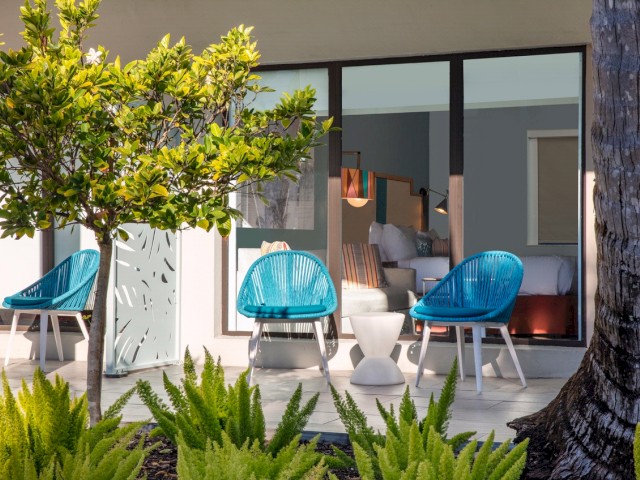 Modern patio with blue chairs, green plants, and sliding glass doors.