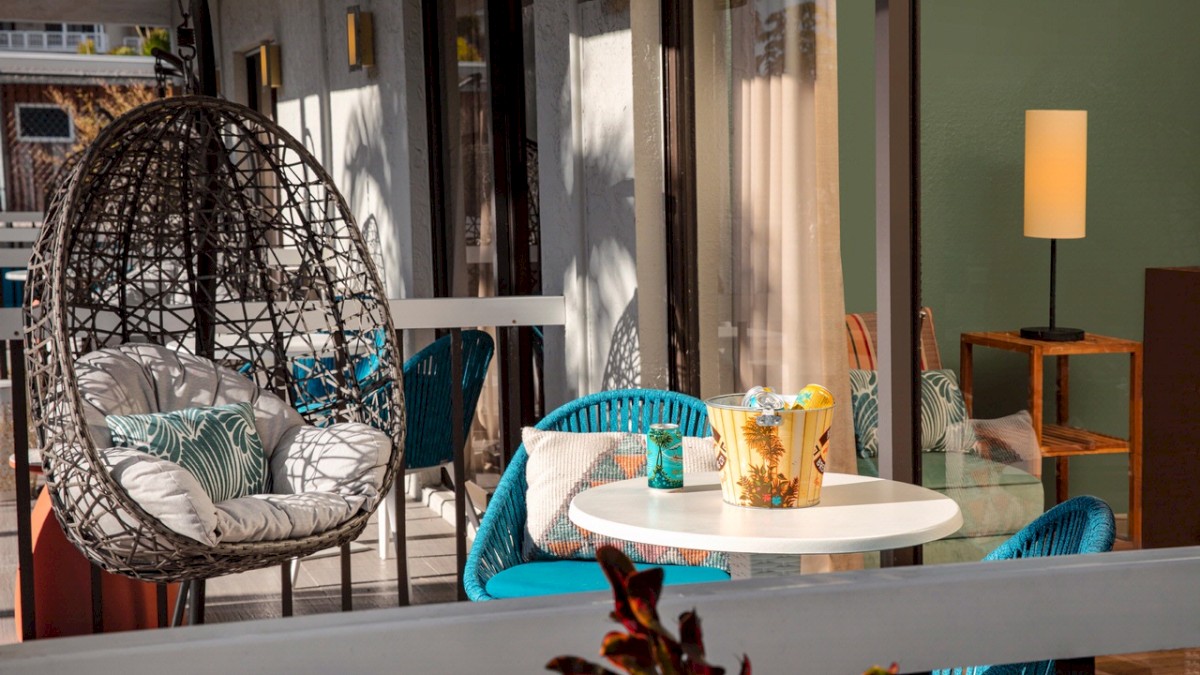 Cozy balcony with a hanging chair, cushions, a table with drinks, and a warm lamp.