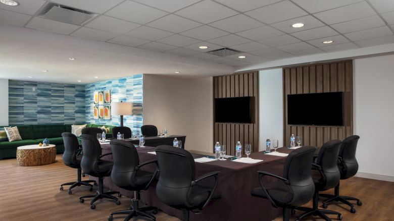 Modern conference room with a large table, chairs, and two TVs on the wall.