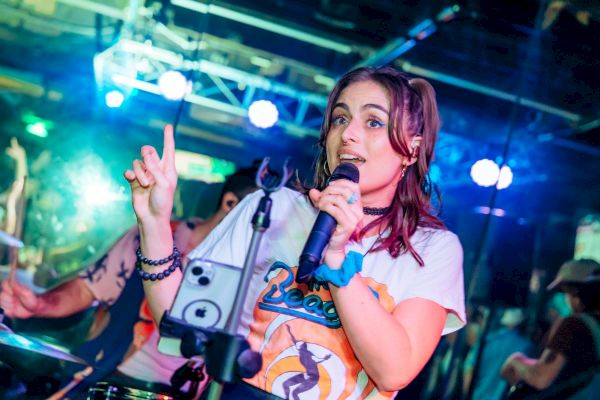 A woman is performing on stage with a microphone, making a peace sign.