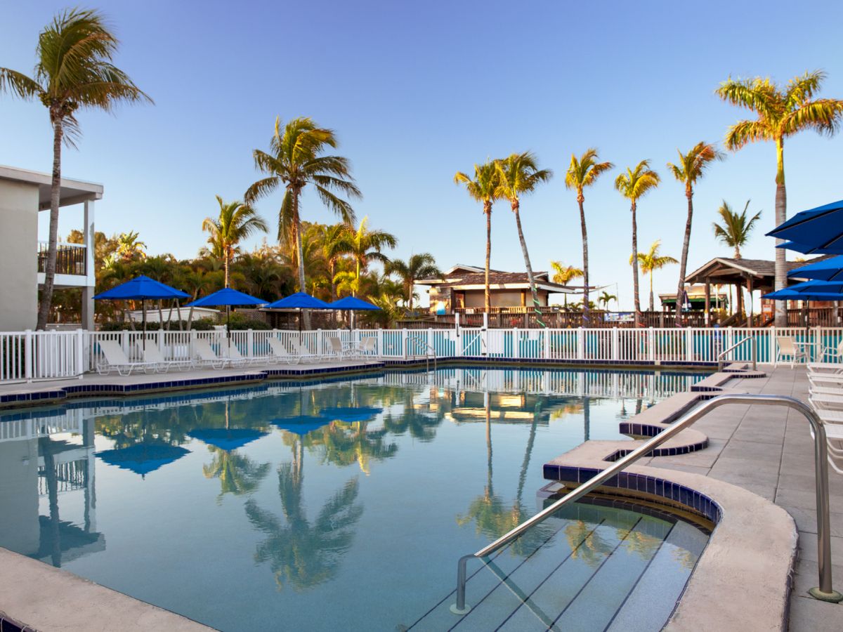 A large serene pool with umbrellas and palm trees reflecting in the water, under a clear sky.