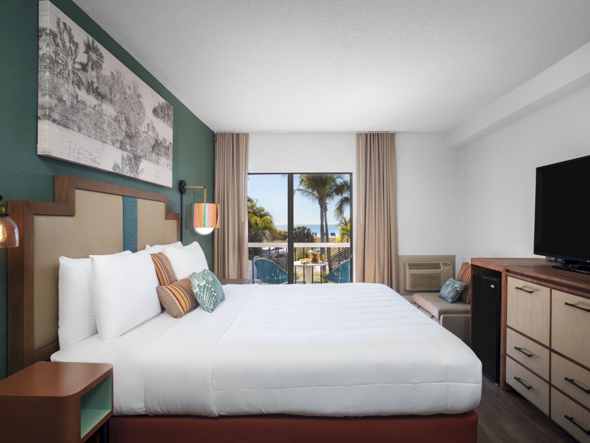 A modern hotel room with a bed, side tables, lamps, and a TV against a window backdrop.