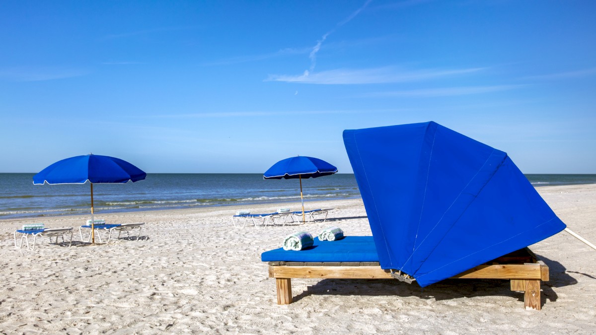 Sandy beach with blue umbrellas and a sunbed under a clear sky.