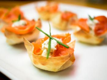 The image shows a plate of appetizing bite-sized appetizers with crispy pastry cups, filled with smoked salmon, cream cheese, and garnished with chives.