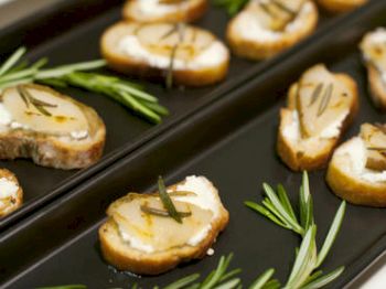 This image shows slices of toasted bread topped with a spread and garnished with herbs, served on black trays with sprigs of rosemary.