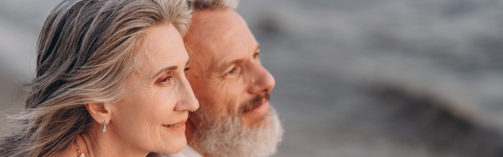 An older couple, looking content, sits close together on a beach, gazing at the ocean. The woman rests her head on the man's shoulder, ending the sentence.