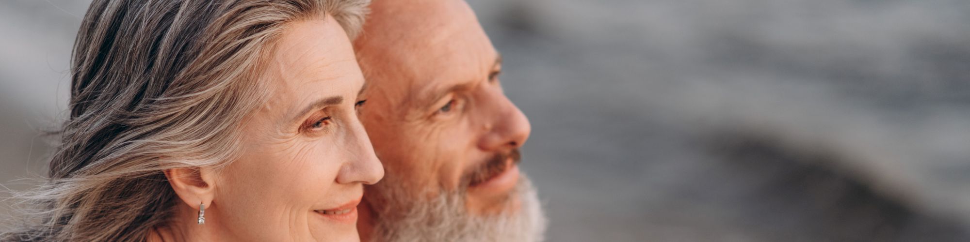 An older couple, looking content, sits close together on a beach, gazing at the ocean. The woman rests her head on the man's shoulder, ending the sentence.