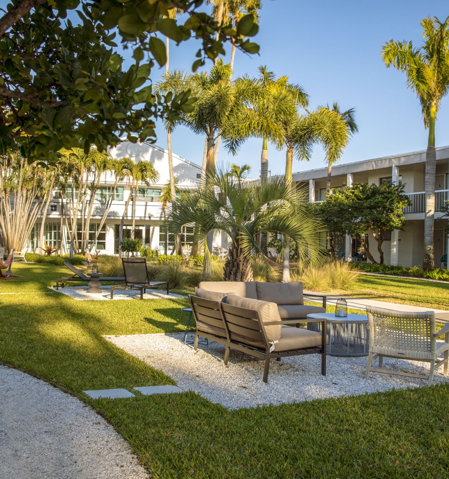 A courtyard with seating areas, palm trees, and a winding pathway in a landscaped garden outside a building.