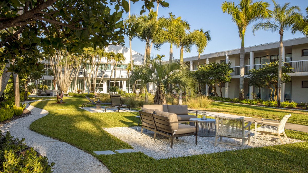 A courtyard with seating areas, palm trees, and a winding pathway in a landscaped garden outside a building.