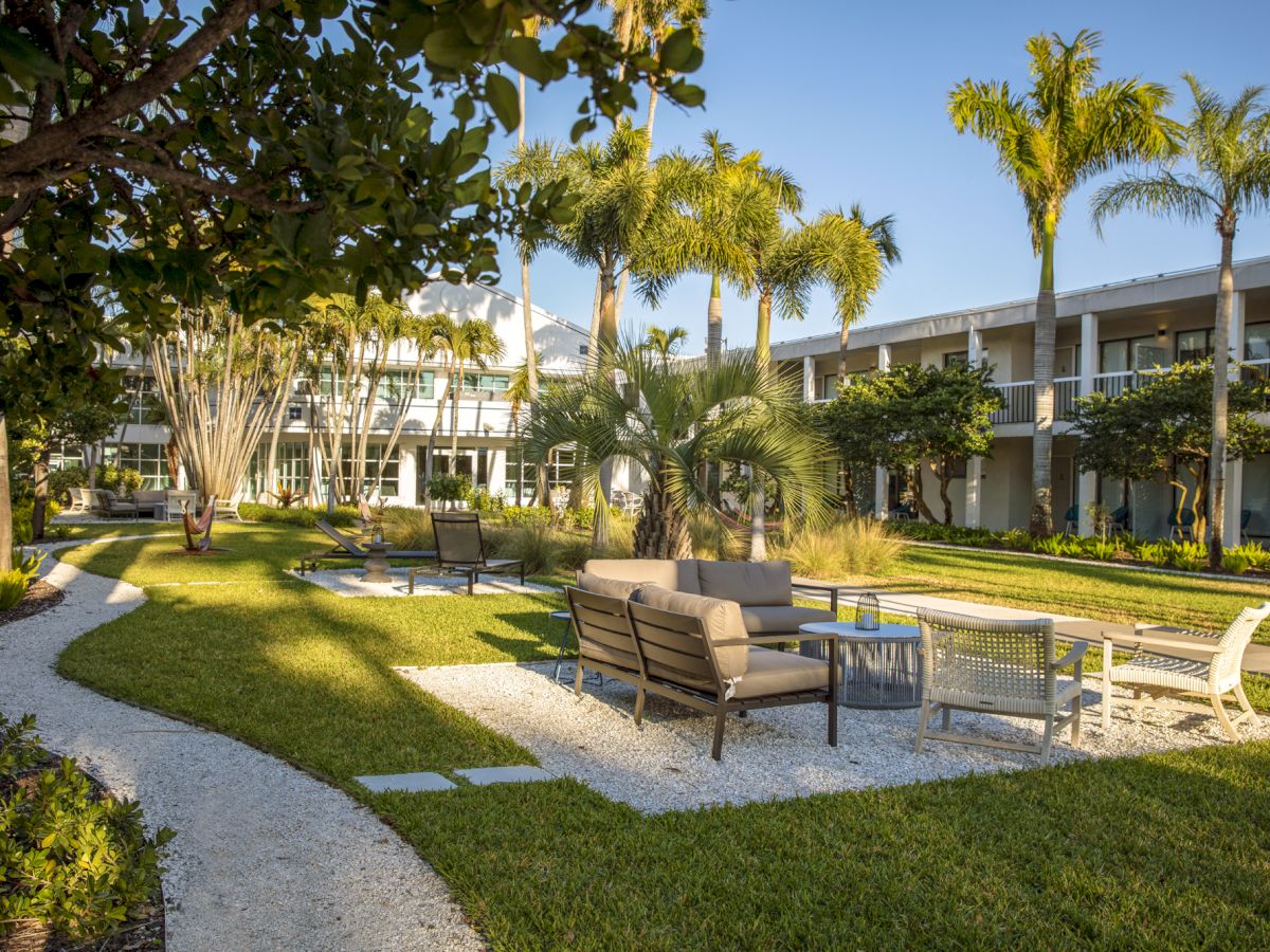 A courtyard with seating areas, palm trees, and a winding pathway in a landscaped garden outside a building.