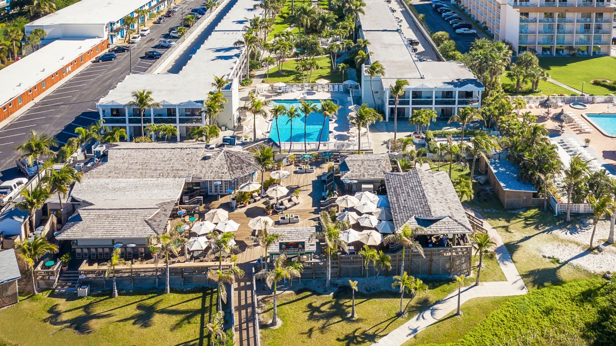 The image shows an aerial view of a Beachcomber Beach Resort with multiple buildings, pools, and outdoor seating areas surrounded by palm trees.