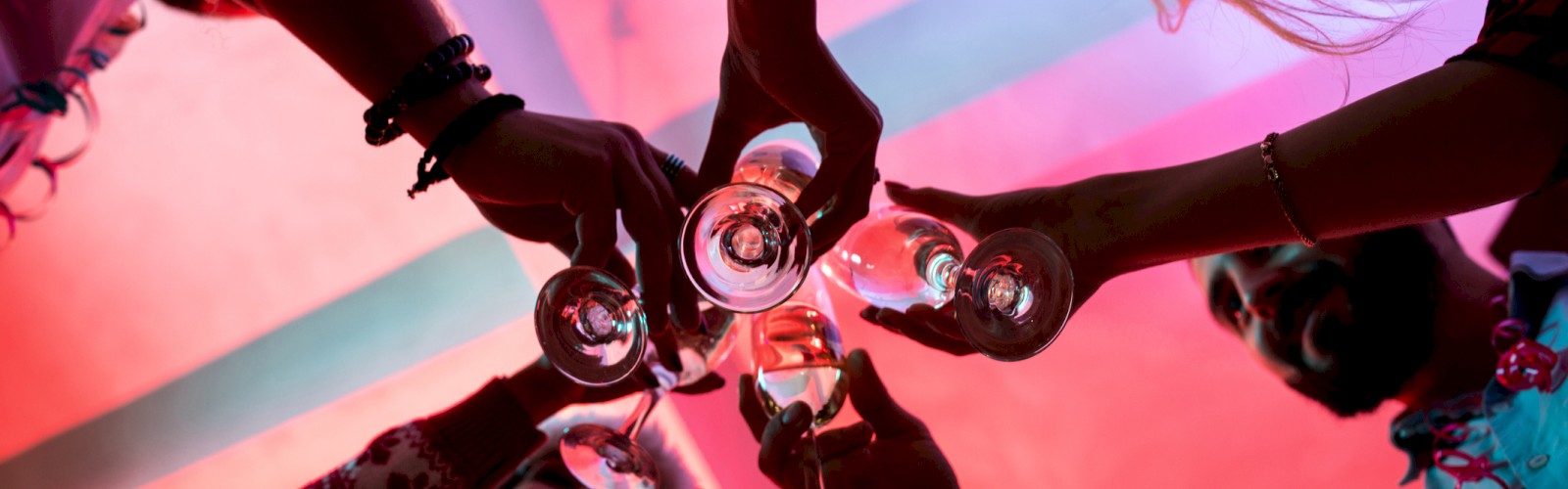 A group of people are raising their glasses for a toast under a red and purple-lit sky.