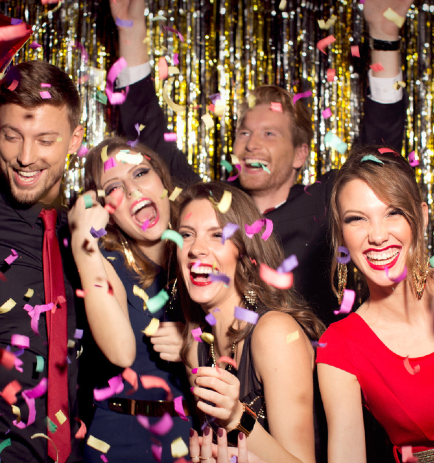 A group of people is celebrating at a party with confetti, gold tinsel backdrop, and smiles, creating a festive and joyful atmosphere.