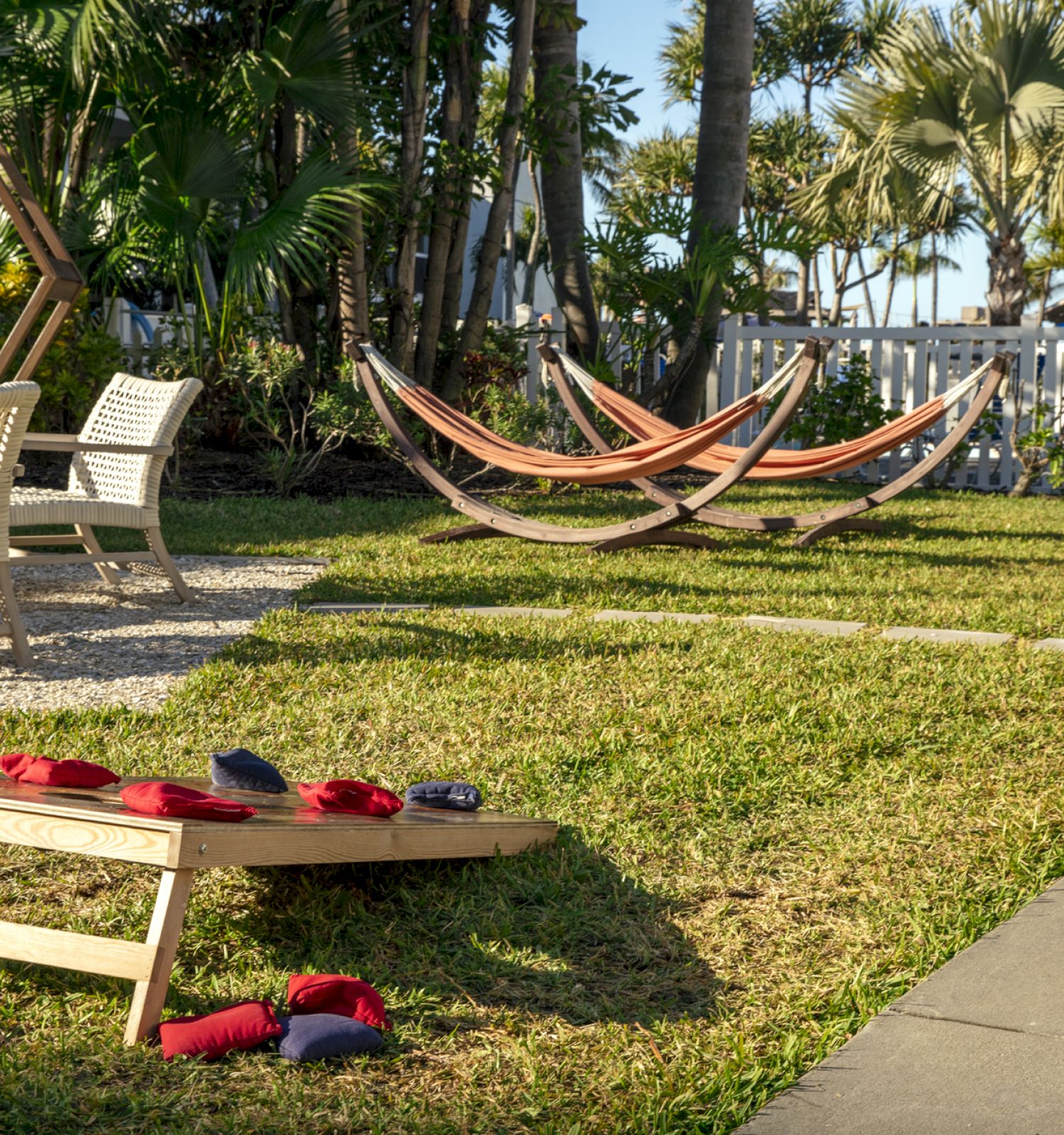 A backyard scene with hammocks, outdoor seating, a cornhole game, and lush greenery. A relaxing outdoor space for leisure and recreation.