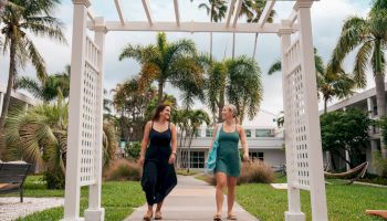 Two ladies walking under a white pergola with greenery around in Beachcomber's courtyard.