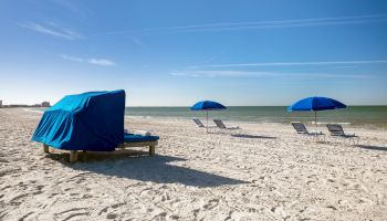 A tranquil beach scene with a covered lounger and open blue umbrellas.