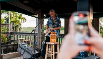 A person is taking a photo of a musician playing guitar on a stage outdoors.