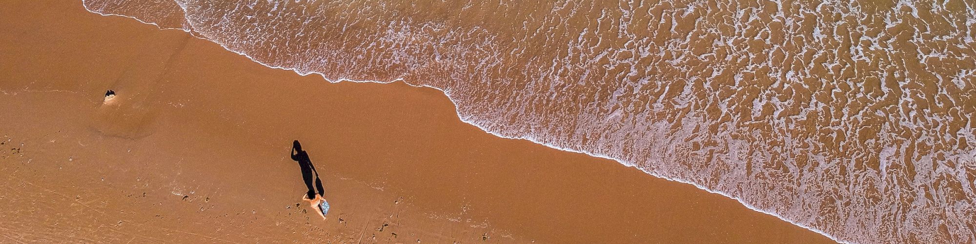 Aerial view of a beach with waves, a person, and sand.