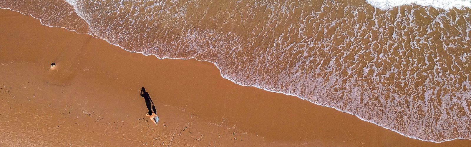 Aerial view of a beach with waves, a person, and sand.