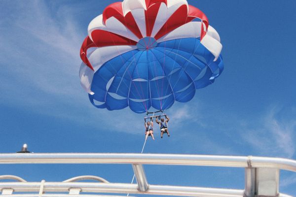 People enjoy parasailing under a blue sky, tethered to a boat with a colorful parachute.