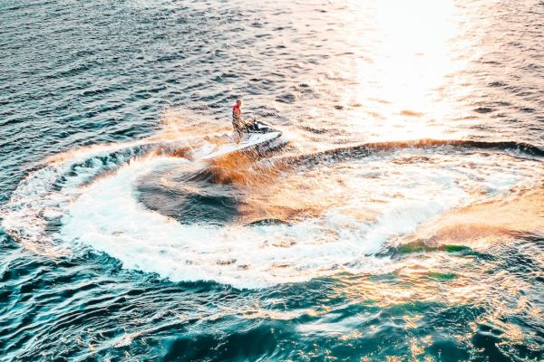 A person is riding a jet ski, creating a circular wave on a sunlit sea.