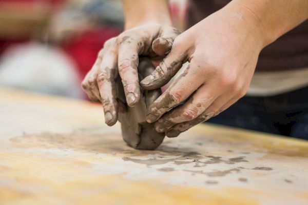 Hands molding clay on a table, crafting pottery with focus and care.