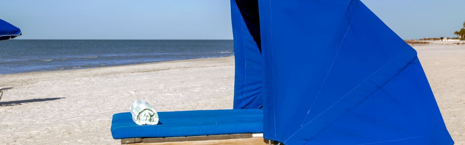 Blue beach chair with a sunshade on sandy beach, clear sky.
